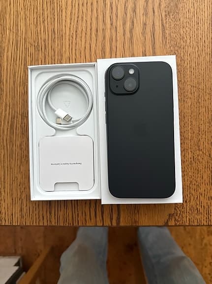 Sort iPhone med æske og ladekabel på et træbord